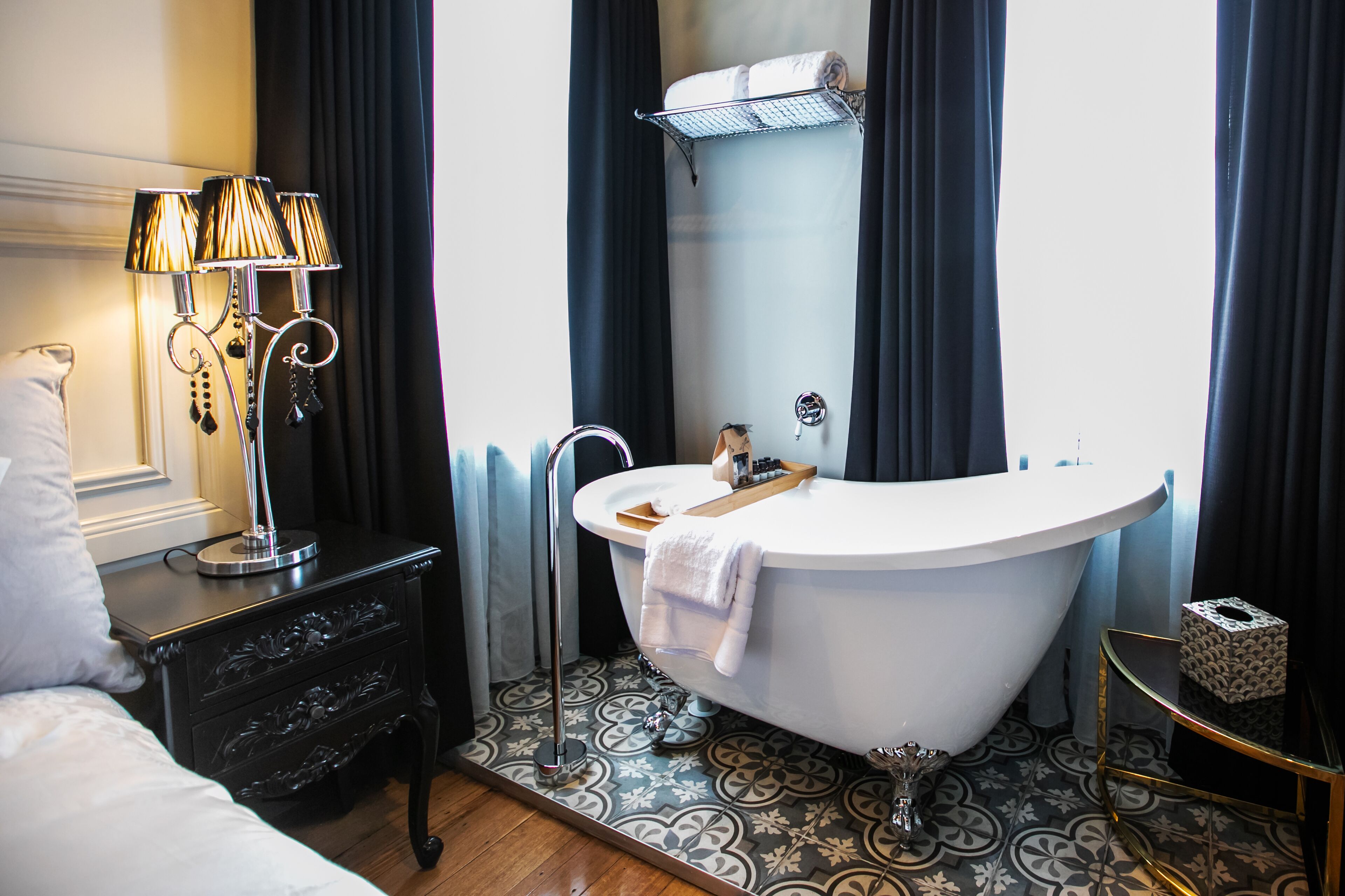 A bathroom with a freestanding bathtub, a vanity with a lamp, and patterned floor tiles.