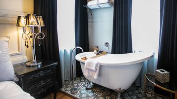 A bathroom with a freestanding bathtub, a vanity with a lamp, and patterned floor tiles.