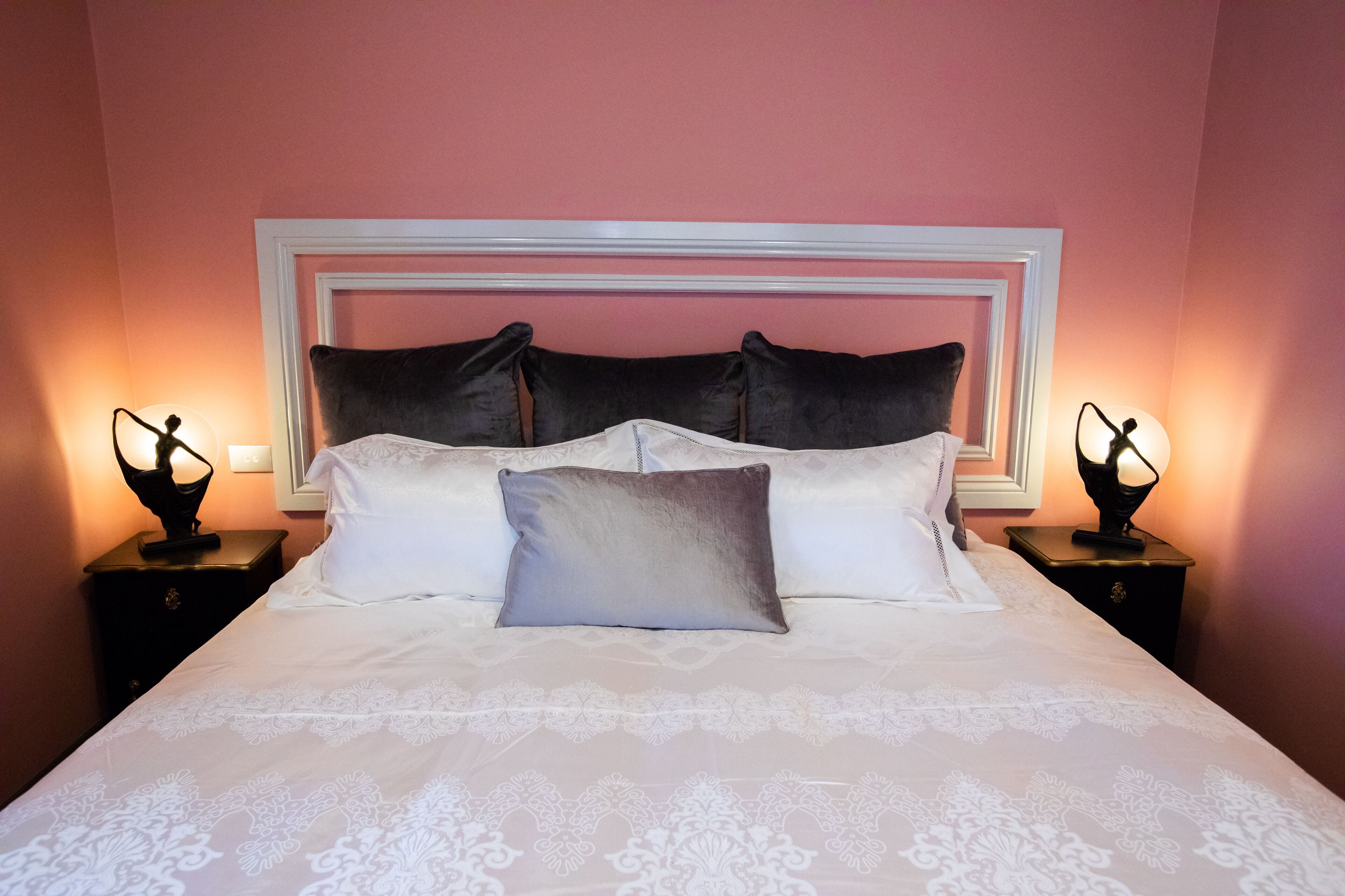 A neatly made bed with a white and grey patterned bedspread, two black nightstands with lamps, and a white headboard.