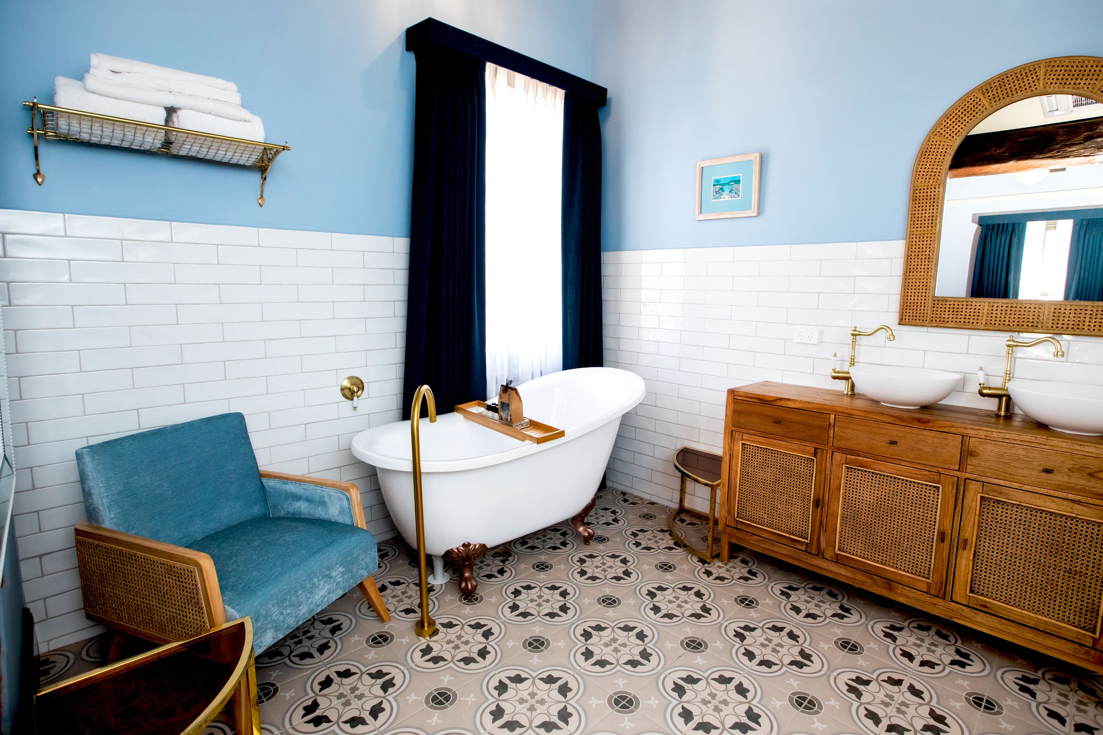 Un baño con una bañera blanca, tocador de madera y una silla azul.