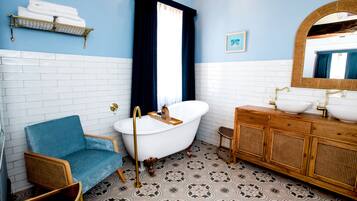 Un baño con una bañera blanca, tocador de madera y una silla azul.