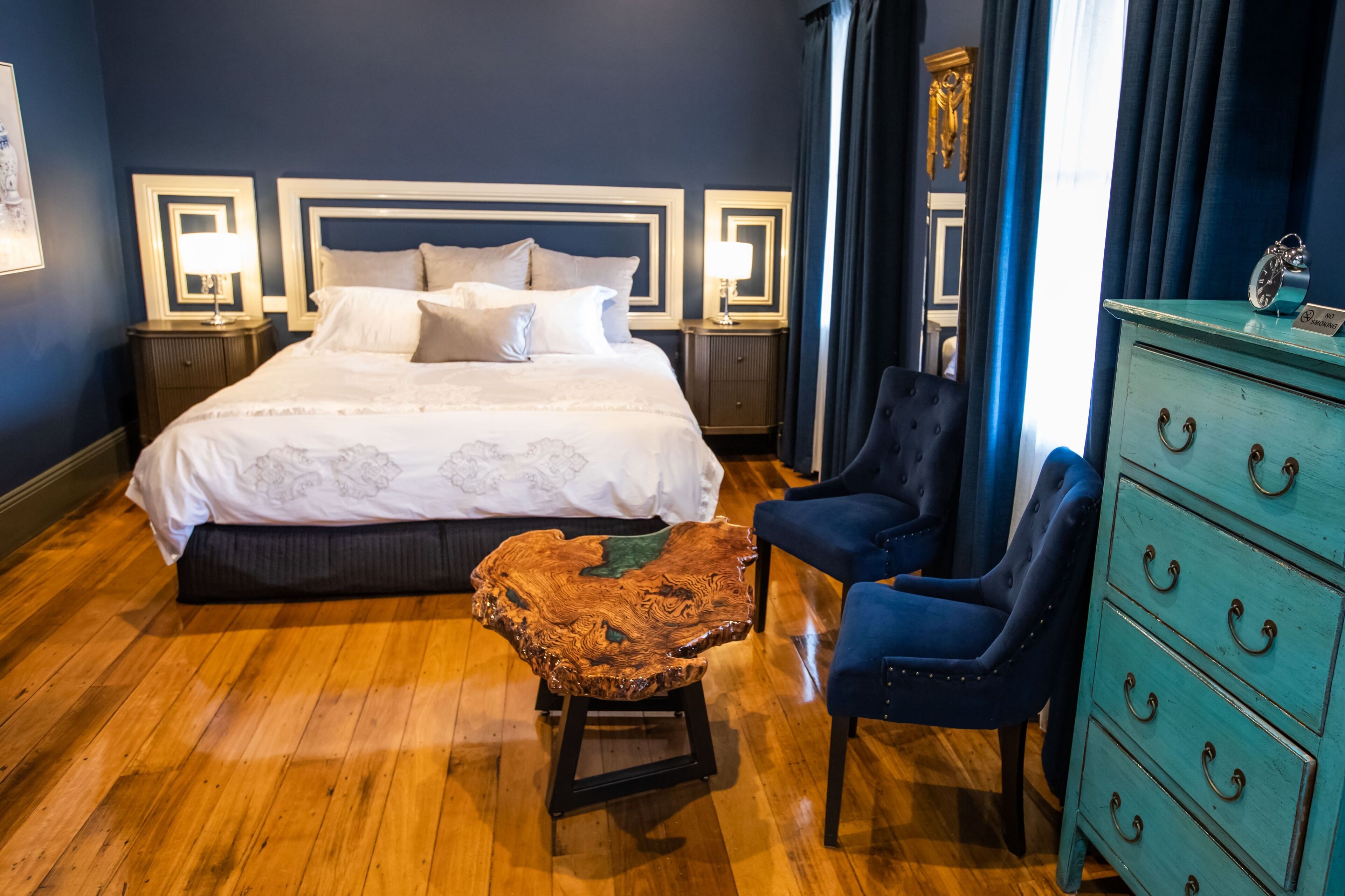 Une chambre d’hôtel avec un grand lit, deux tables de chevet, une table basse en bois, deux fauteuils et une commode.