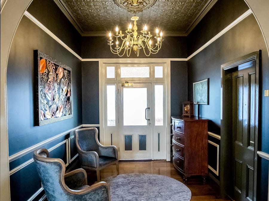 A hallway with a chandelier, two armchairs, a round rug, and a wooden cabinet.