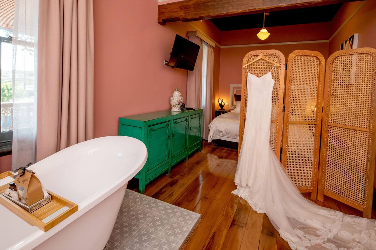 A bedroom with a large bathtub, a green dresser, a bed with a white canopy, and a television on the wall.