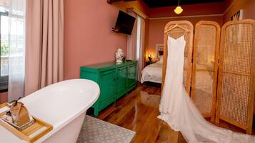 Un dormitorio con una bañera grande, un aparador verde, una cama con dosel blanco y un televisor en la pared.