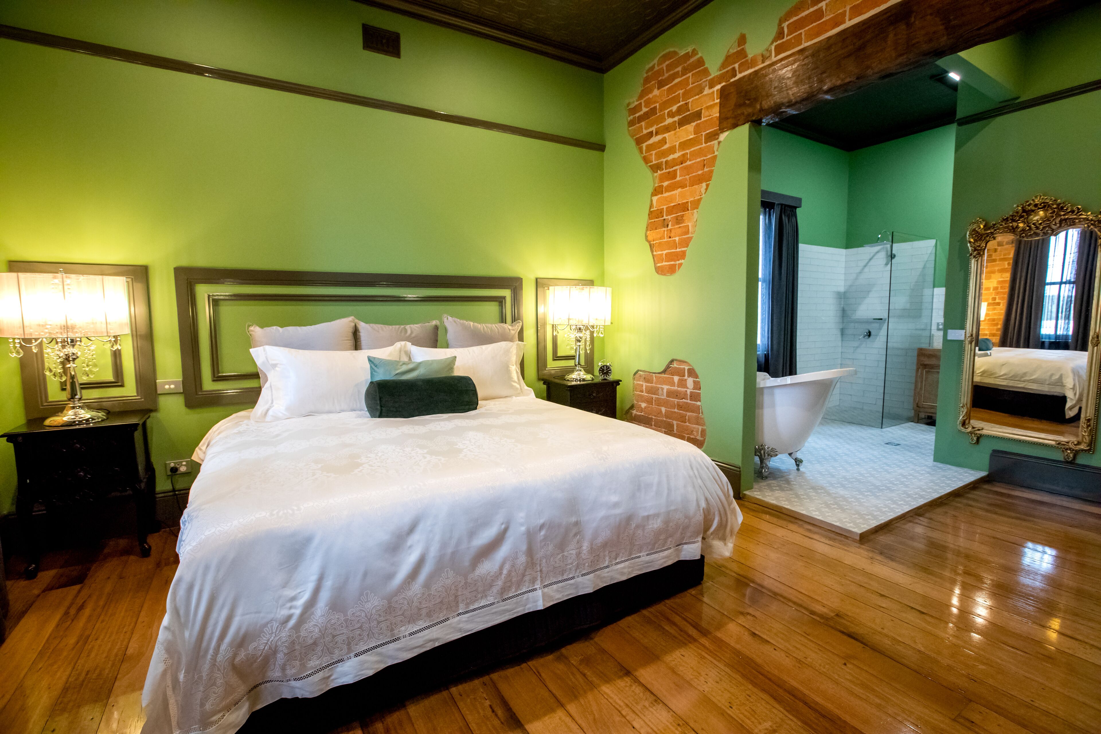 Habitación de hotel con una cama grande, dos lámparas de noche, una pared de ladrillo, una bañera y un espejo.