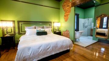 Habitación de hotel con una cama grande, dos lámparas de noche, una pared de ladrillo, una bañera y un espejo.