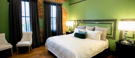 A hotel room with a large bed, two chairs, a brick wall, and green walls.