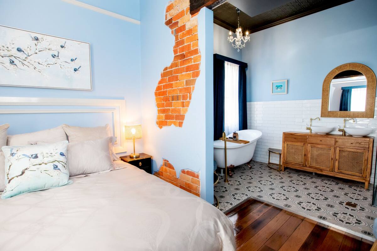 A bedroom with a large bed, a nightstand with a lamp, and a wall with a brick design.