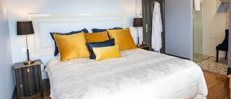 A neatly made bed with a white and gold bedspread, two nightstands with lamps, and a door with a towel hanging on it.