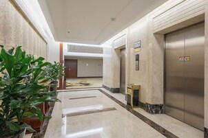 Un pasillo de hotel con piso de mármol, plantas en macetas, un mostrador de recepción y un ascensor.