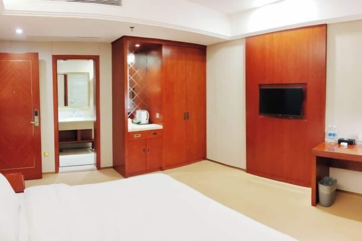 Hotellihuone, jossa on sänky, vaatekaappi, peilillä varustettu meikkipöytä, televisio ja työpöytä.