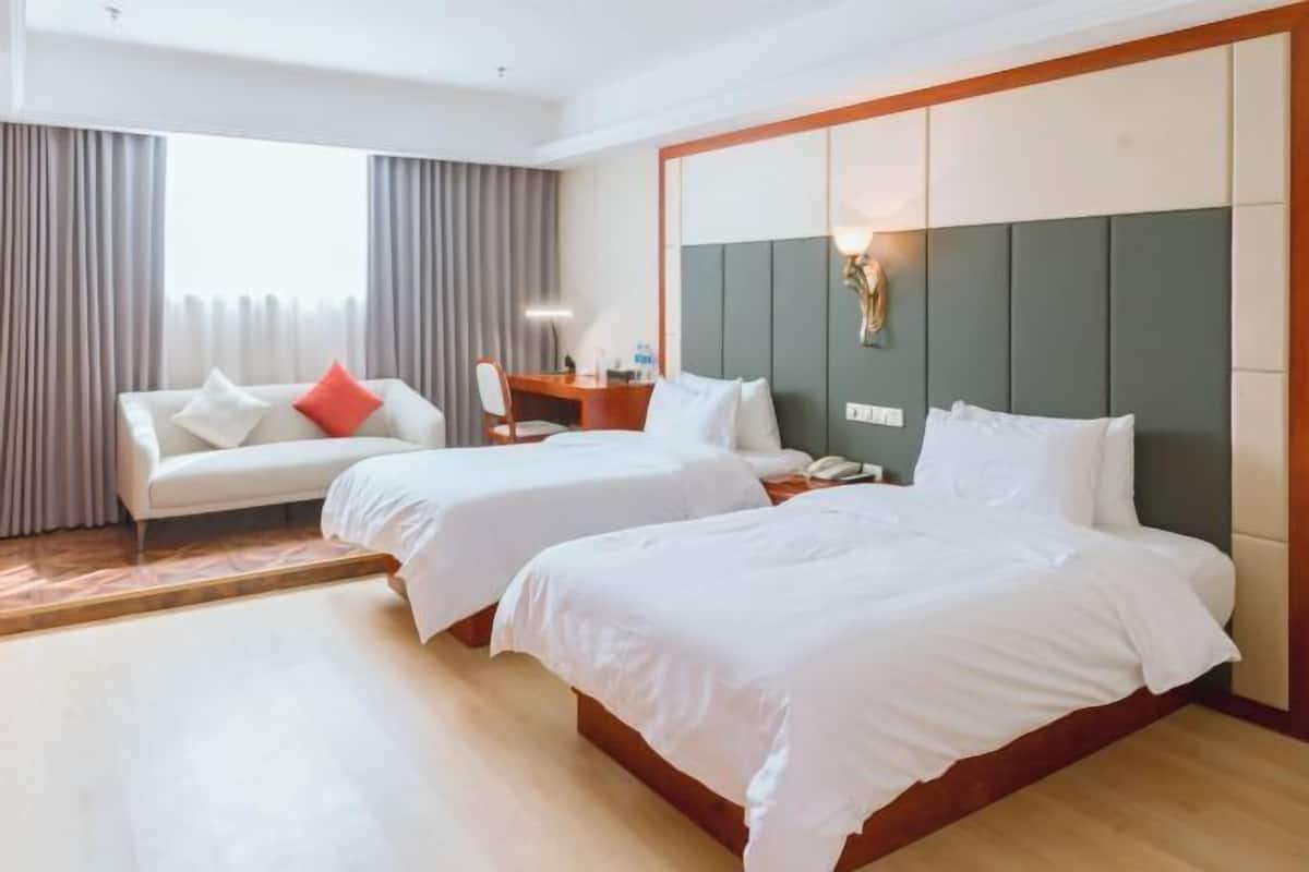 Hotellihuone, jossa on kaksi sänkyä, sohva, työpöytä ja suuri ikkuna, jossa on verhot.