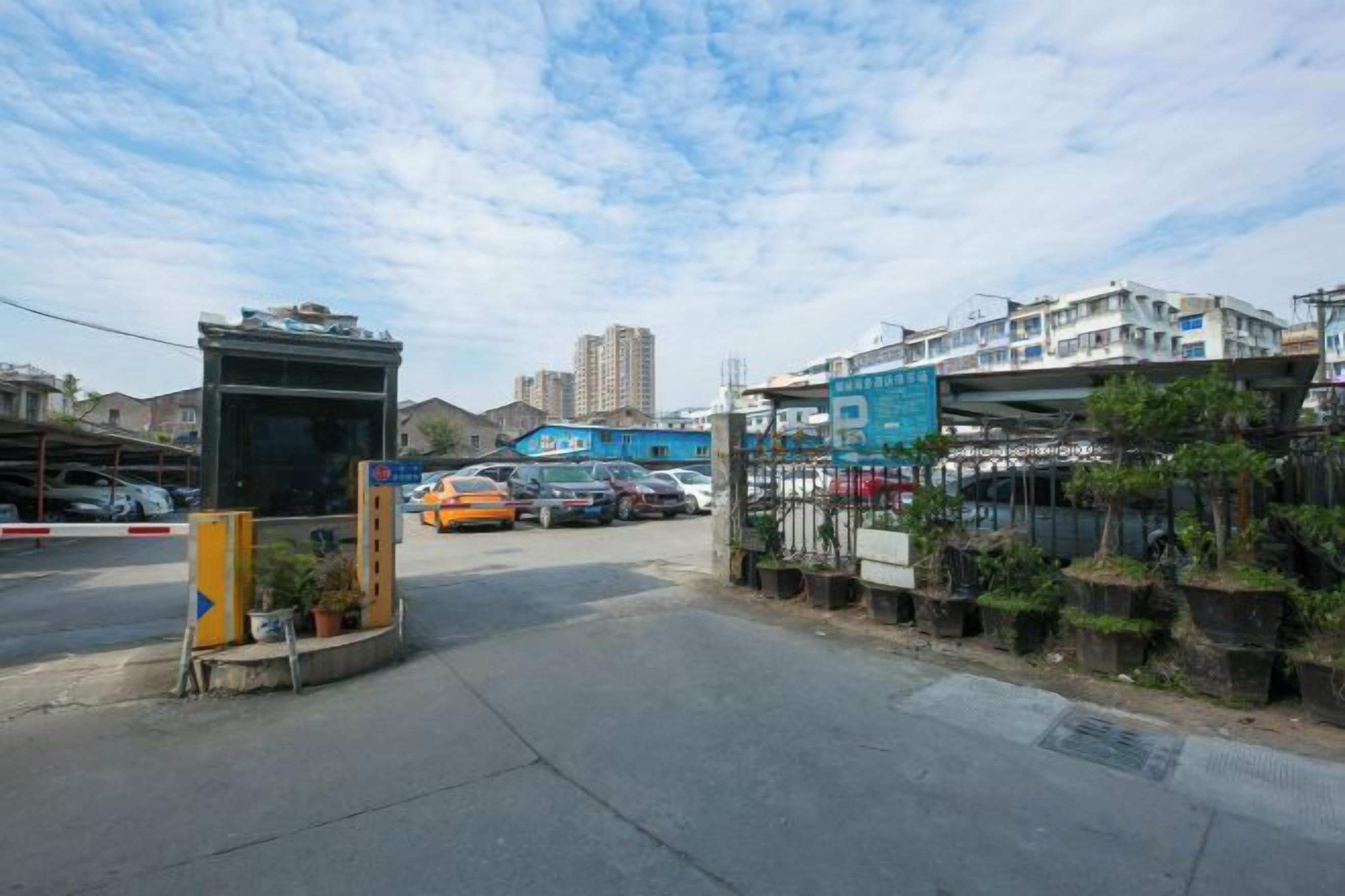 A street view with a parking area, a building with a blue sign, and a pedestrian overpass.