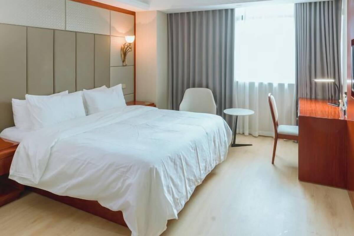Hotellihuone, jossa on suuri sänky, pieni pyöreä pöytä, tuoli ja työpöytä.