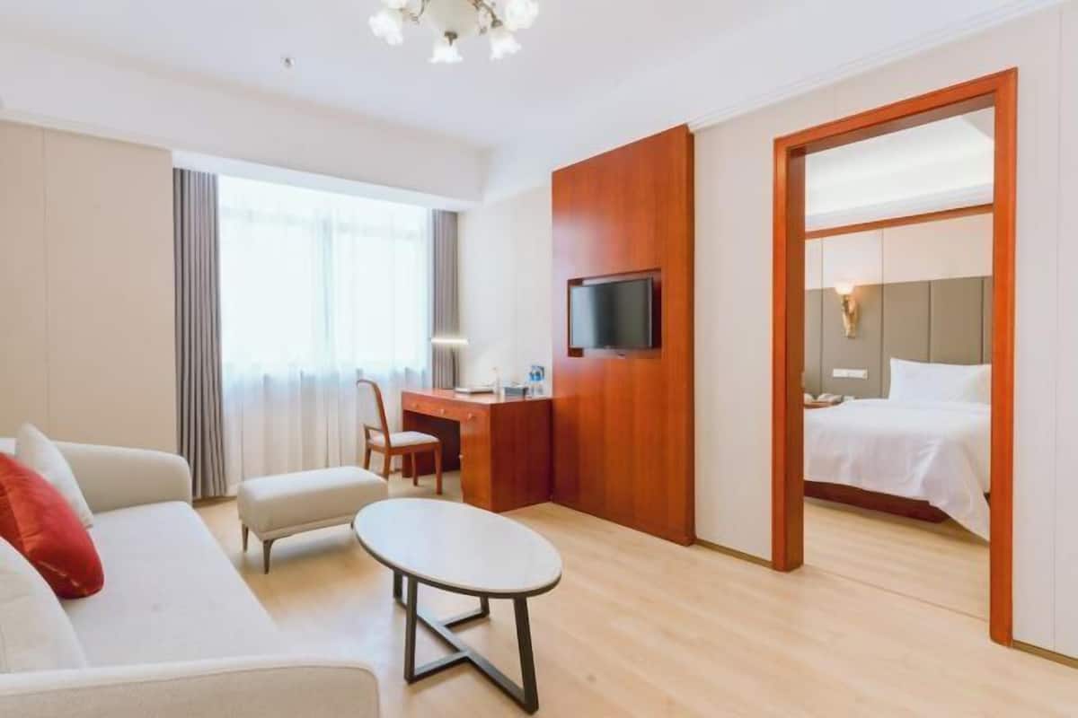 Hotellihuone, jossa on sohva, pieni pöytä, kirjoituspöytä, jossa on televisio, ja sänky.