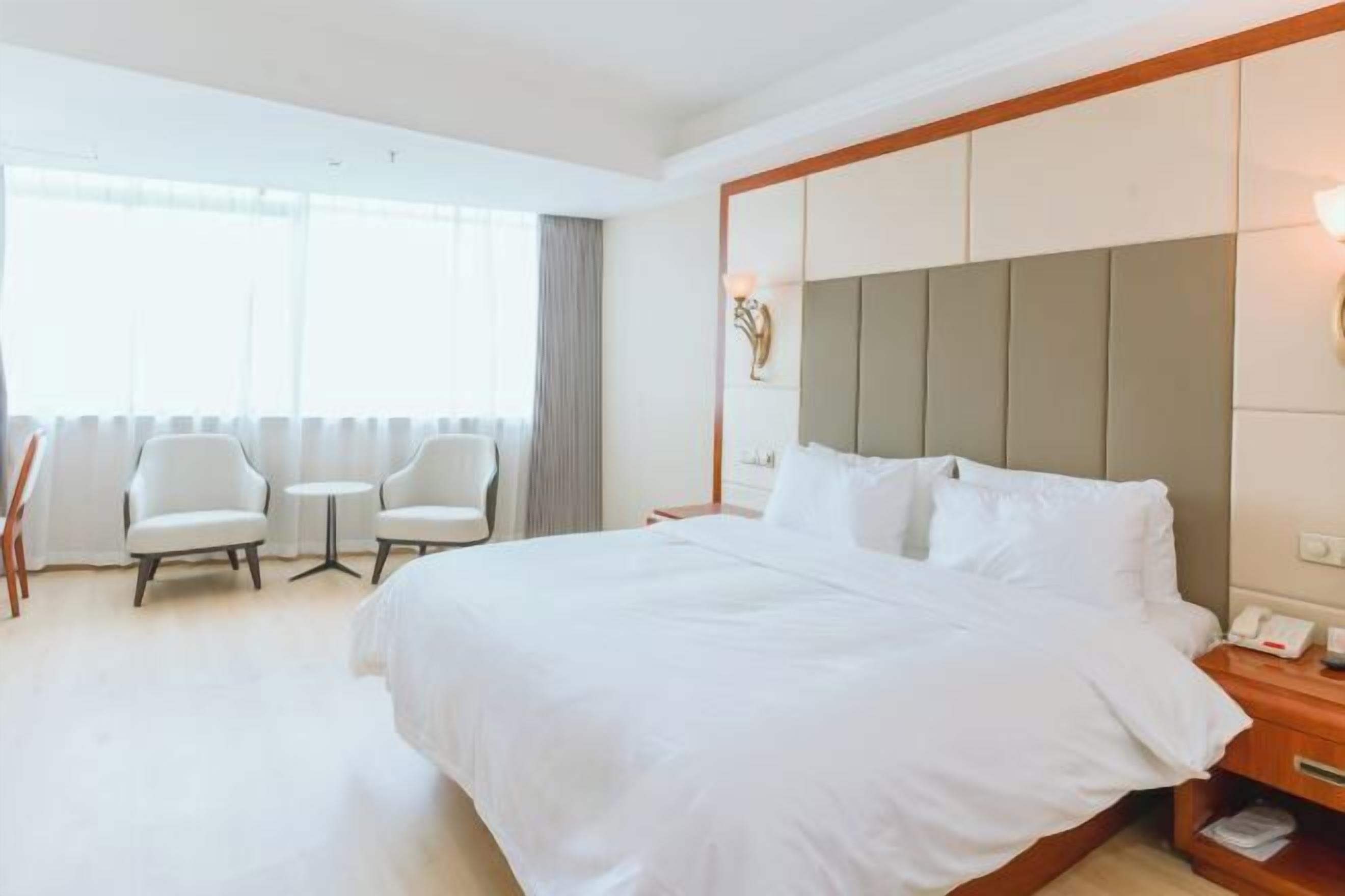 A hotel room with a large bed, two armchairs, a small table, and a nightstand with a phone.