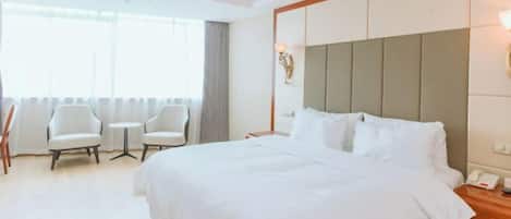 A hotel room with a large bed, two armchairs, a small table, and a nightstand with a phone.