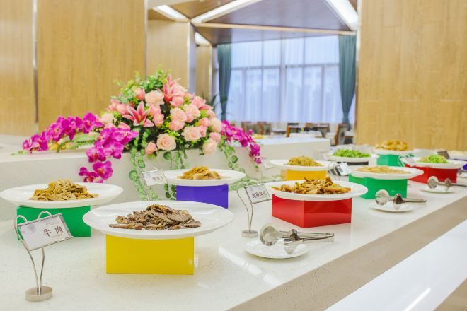 A buffet table with various dishes in colorful containers, a floral centerpiece, and a sign indicating a meat dish.