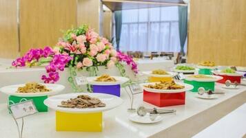 A buffet table with various dishes in colorful containers, a floral centerpiece, and a sign indicating a meat dish.