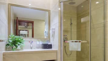A modern bathroom with a glass-enclosed shower, a large mirror, and a vanity with a plant and toiletries.
