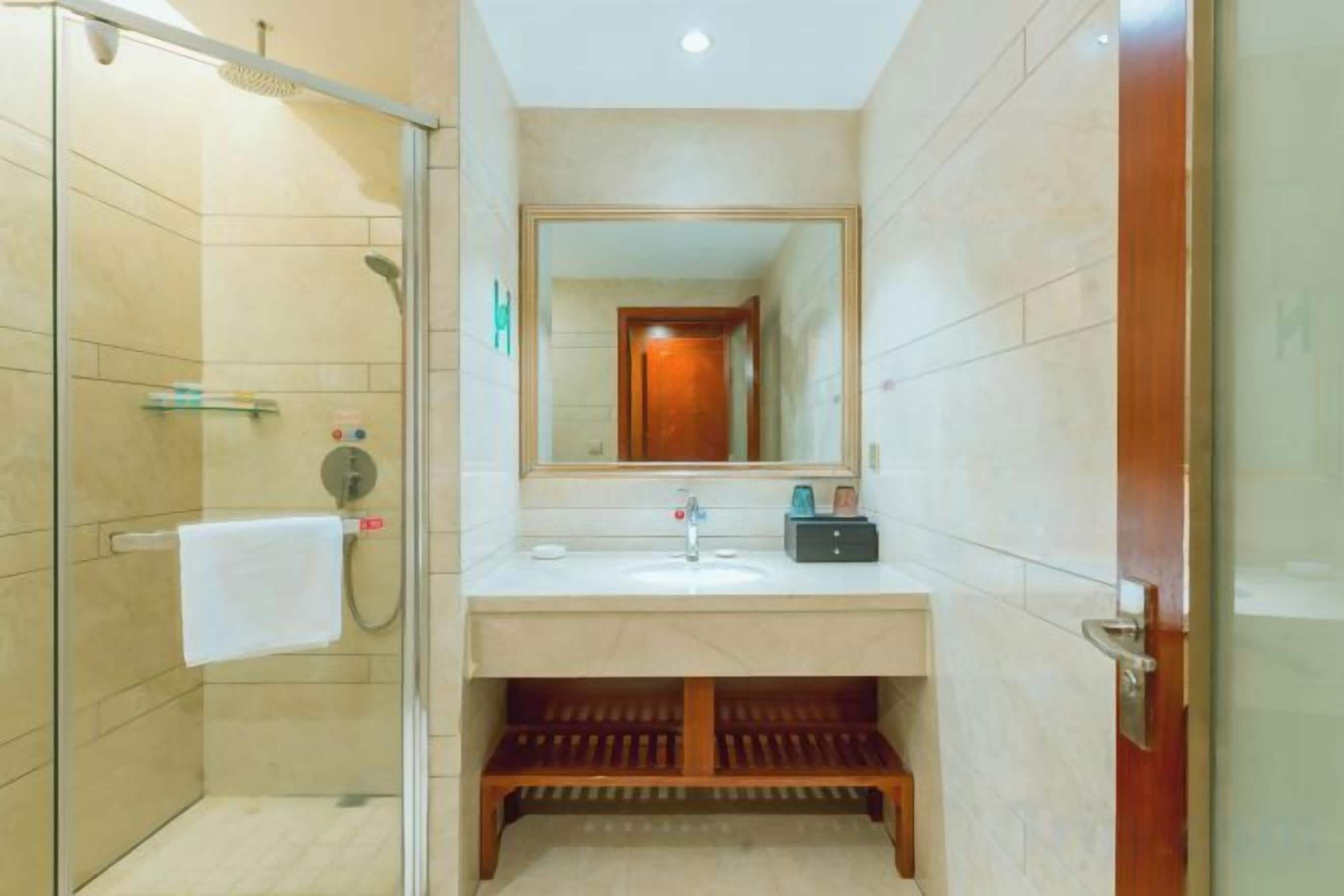 A bathroom with a glass shower enclosure, a sink with a mirror above it, and a wooden vanity.