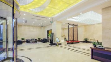 A spacious lobby with a modern design, featuring a reception desk, seating area, and a large chandelier.