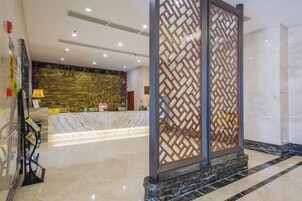 Zona de recepción de un hotel con mostrador de mármol, una pantalla decorativa y un mostrador de recepción.