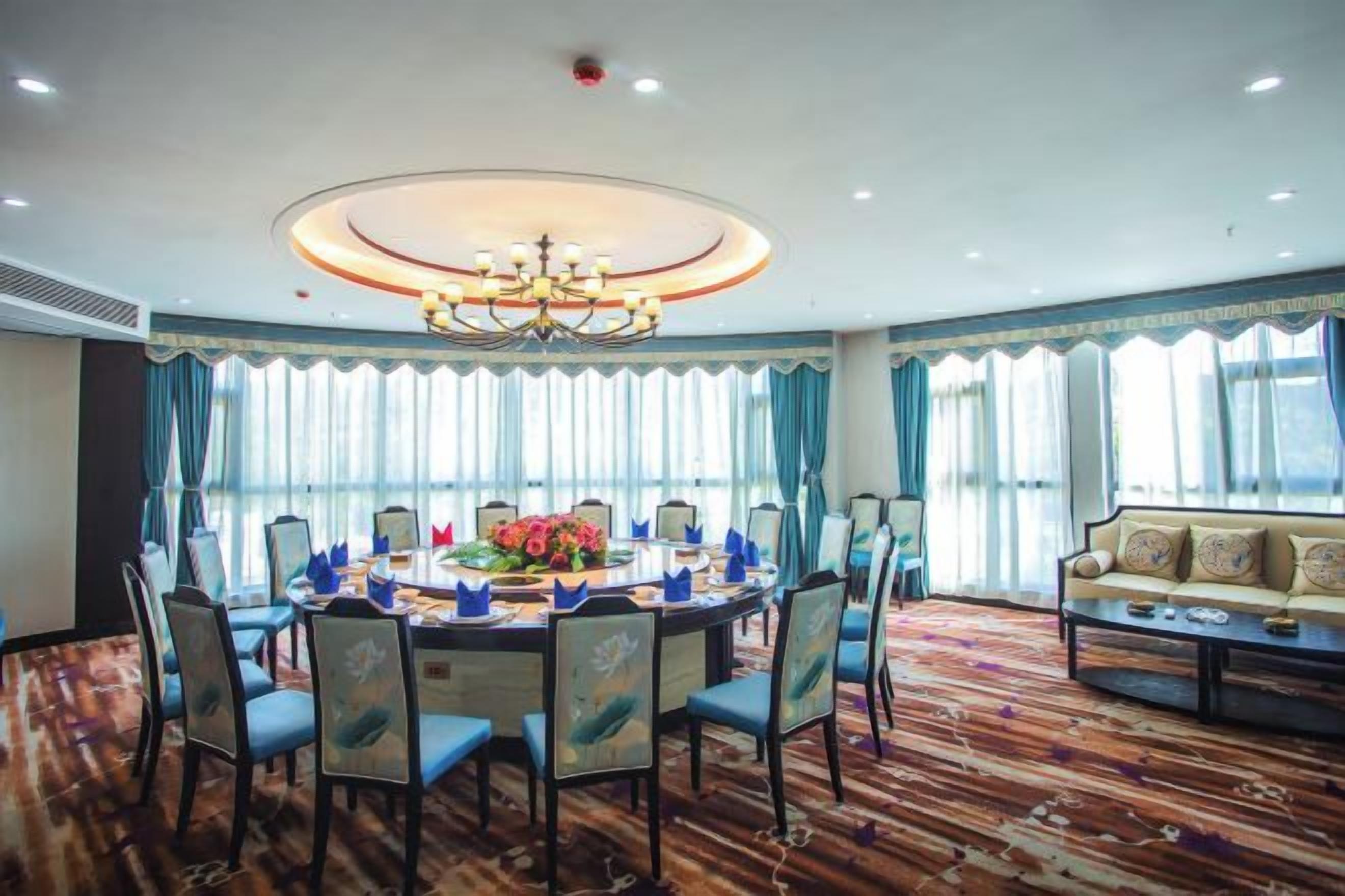 A conference room with a round table, chairs, a sofa, and a chandelier.