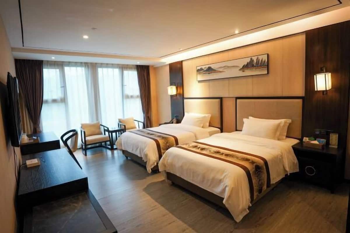 A hotel room with two beds, a desk, a chair, and a large window with curtains.