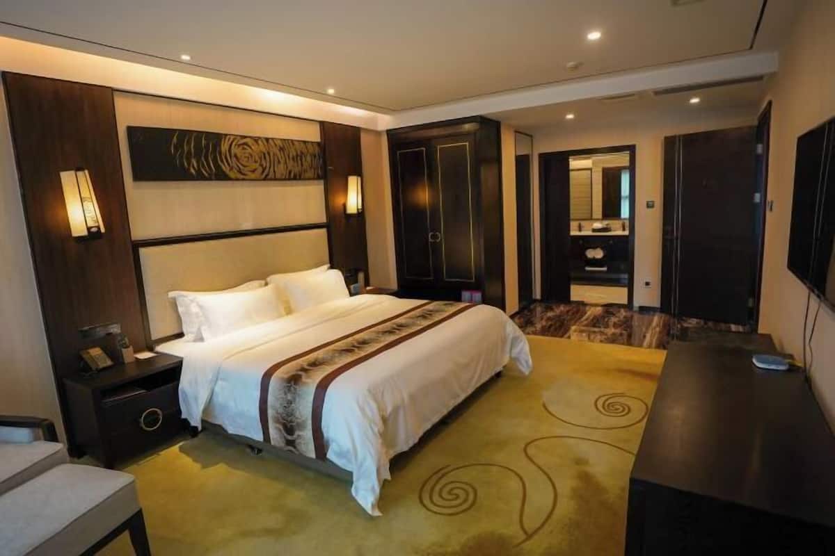 A hotel room with a large bed, a desk, a nightstand, a mirror, and a TV.