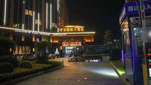 A hotel entrance with illuminated signage, a covered walkway, and a parked bus. - Jun'an International Hotel (Cenxi)