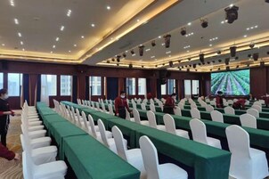 A conference room with rows of tables, white chairs, and a large screen at the front.