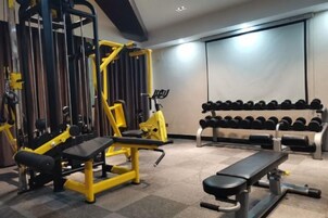 Un gimnasio con equipo de levantamiento de pesas, mancuernas y bancos.