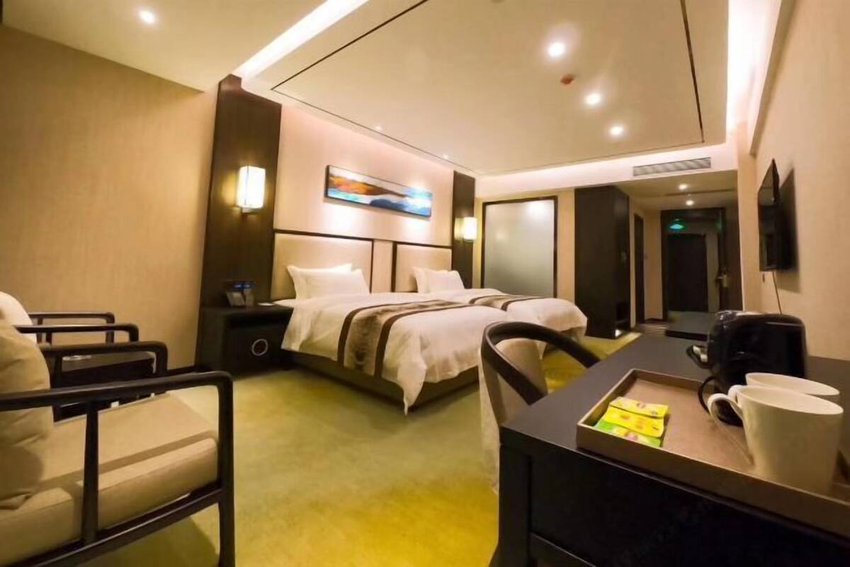 A hotel room with a bed, bedside tables, a desk with a chair, a coffee maker, and a tray with items.