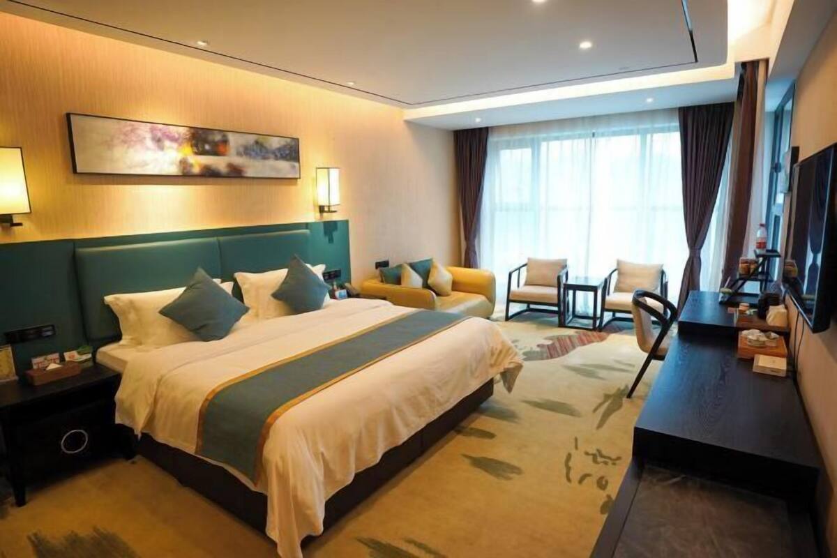 A hotel room with a large bed, a desk, a chair, and a window with curtains.