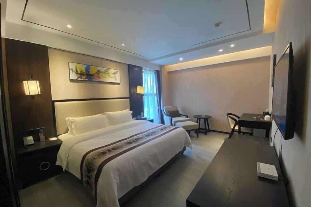 A hotel room with a bed, bedside table, lamp, chair, desk, and TV.