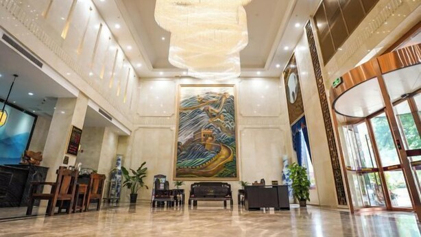 A spacious lobby with a large mural, a reception desk, and a chandelier. - Jun'an International Hotel (Cenxi)