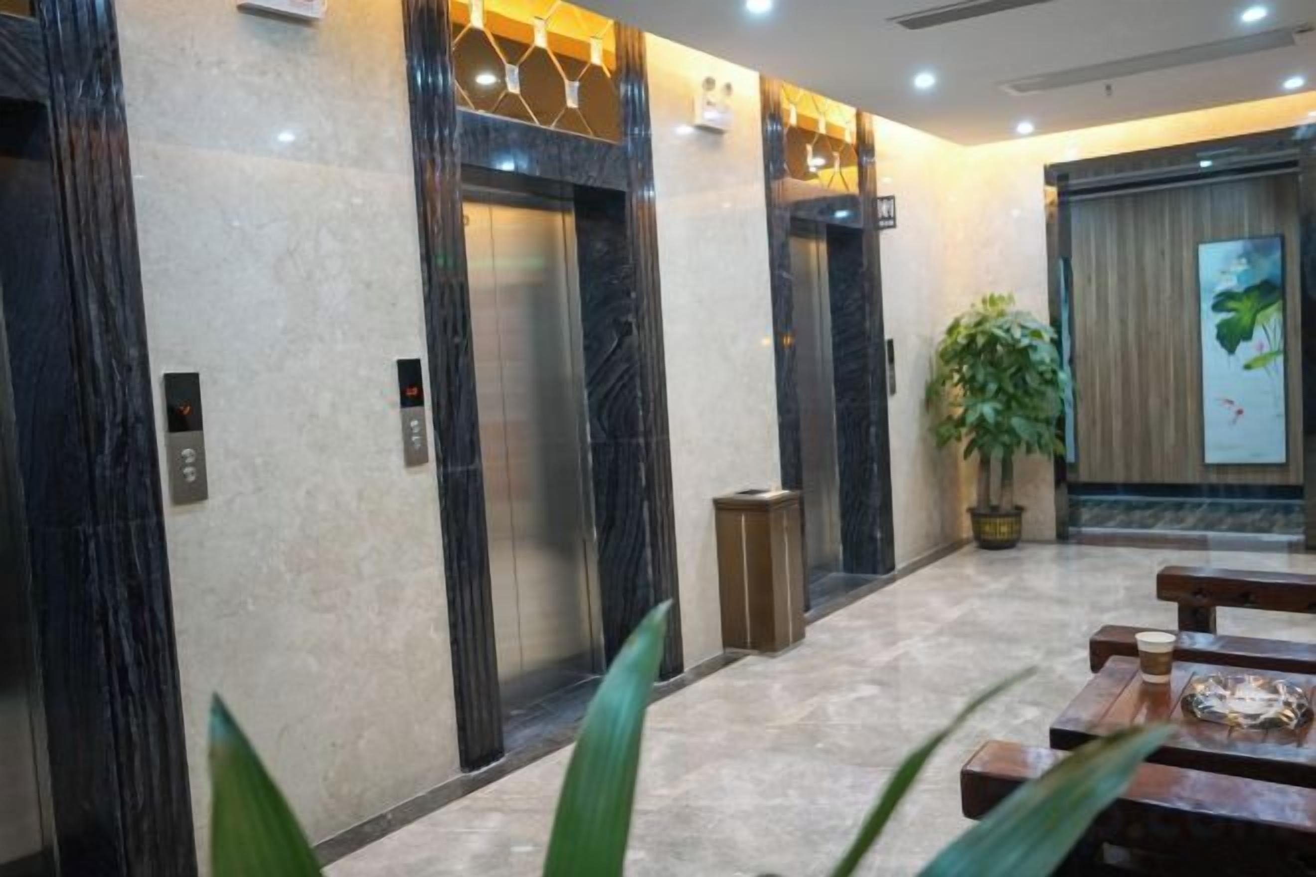 Un vestíbulo con pisos de mármol, dos ascensores, una planta en maceta y un banco de madera.