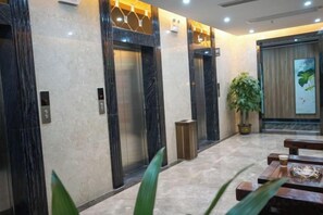 A lobby with marble flooring, two elevators, a potted plant, and a wooden bench. - Jun'an International Hotel (Cenxi)