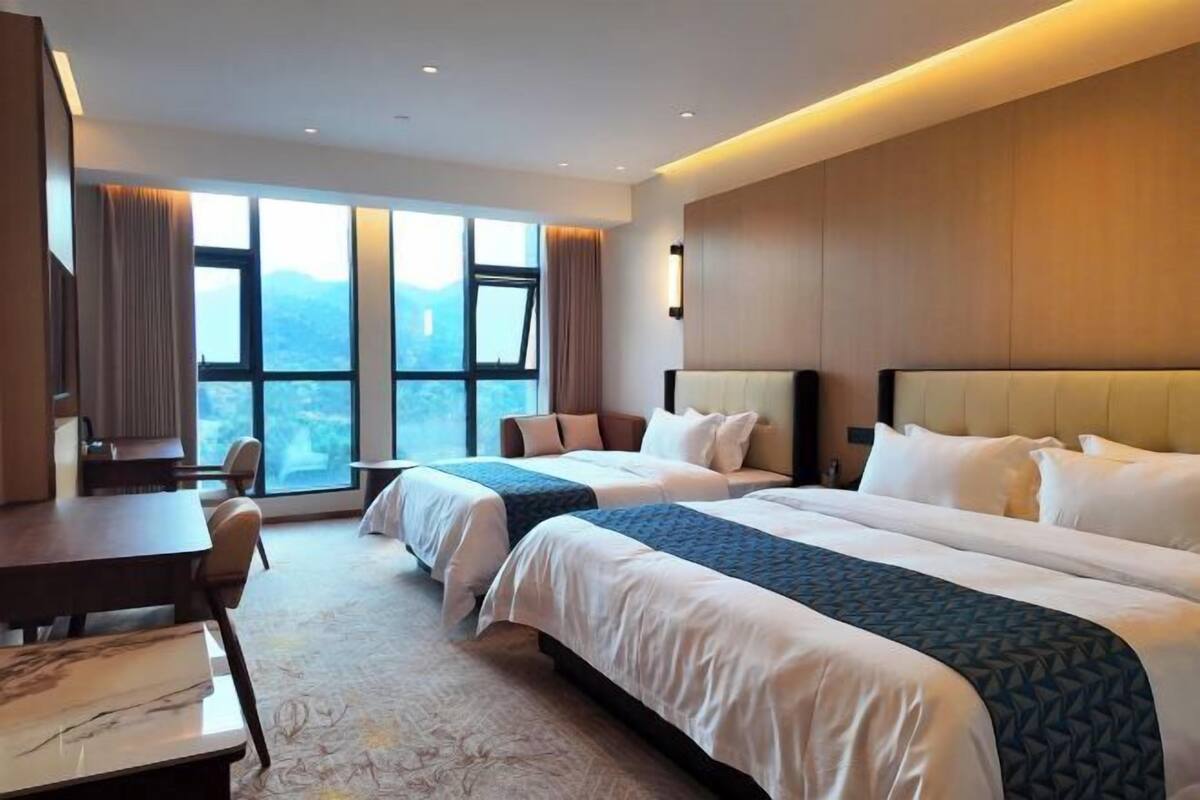 A hotel room with two beds, a desk, and a view of the mountains through large windows.