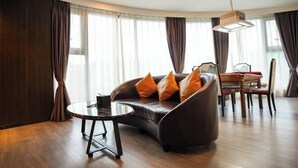 A modern living room with a curved sofa, a round coffee table, and a dining area with a wooden table and chairs. - Jun'an International Hotel (Cenxi)