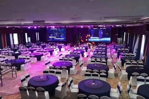 A conference room with round tables and chairs, a stage with a large screen, and a carpeted floor. - Jun'an International Hotel (Cenxi)