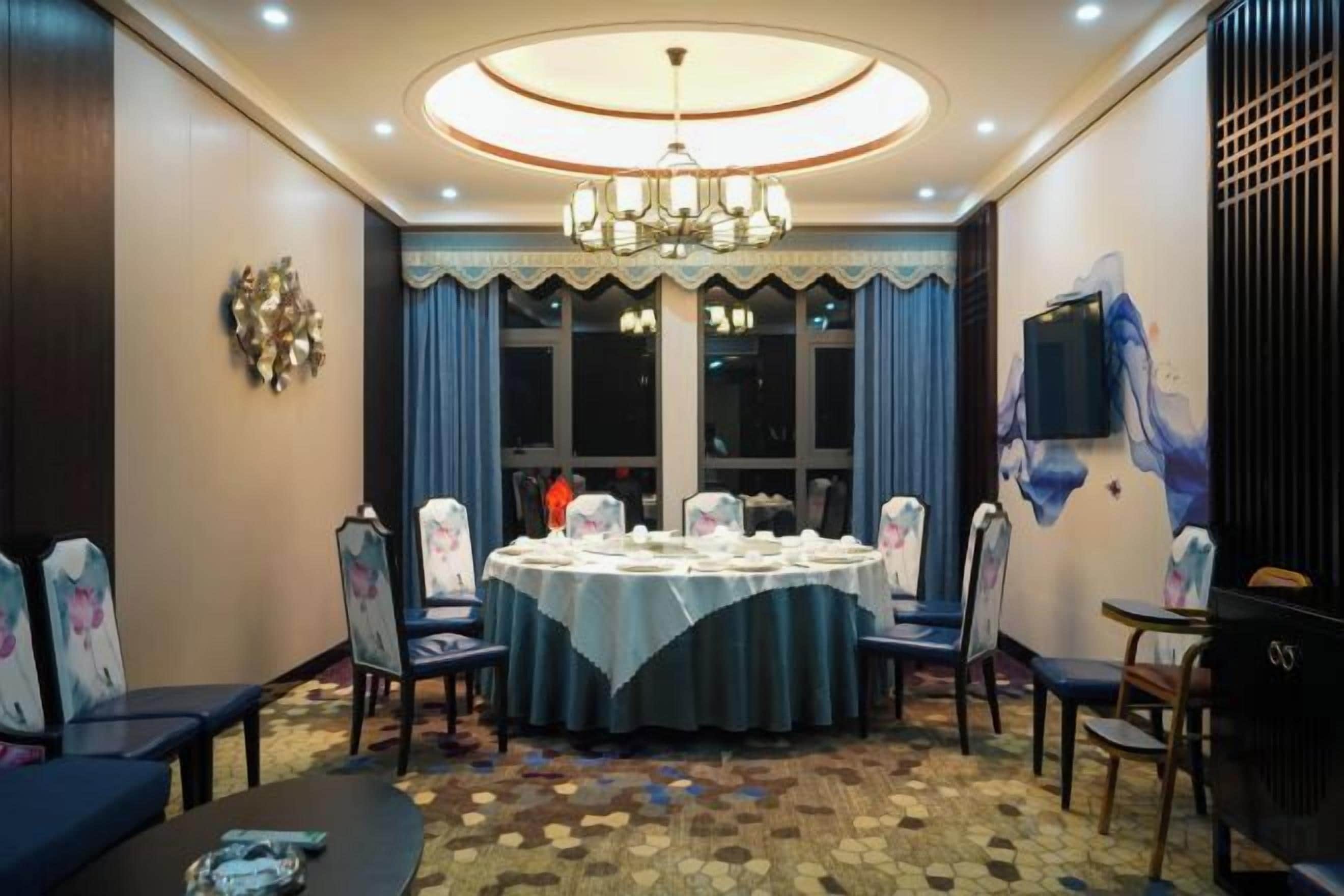A conference room with a round table, chairs, a chandelier, and a large window with curtains.