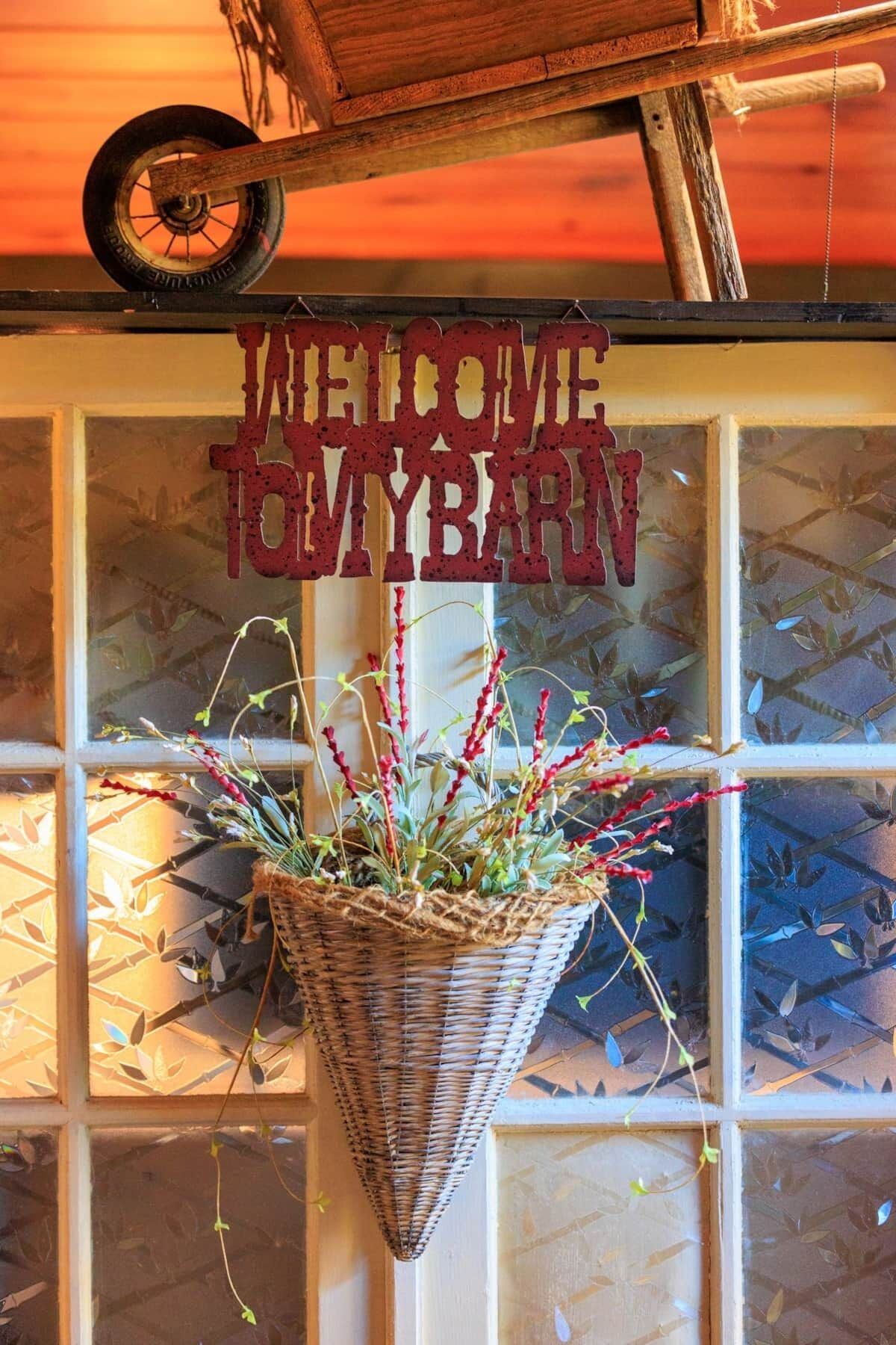 A welcome sign above a window with a hanging basket of plants.