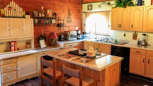 A rustic kitchen with wooden cabinets, a central island, and a dining area with chairs. - The Ole Pole Barn at Dry Creek Hideaways (Middle Valley)