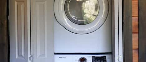 A front view of a laundry room with a Samsung washer and dryer, wooden walls, and a door with a painting above it.
