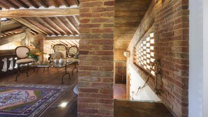 A rustic interior with exposed wooden beams, brick walls, and a traditional wooden staircase. - Il Romitoio 12 (Castiglion Fiorentino)
