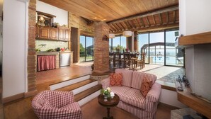 A spacious living area with a fireplace, a dining area with a view, and a kitchen with wooden cabinets. - Il Romitoio 12 (Castiglion Fiorentino)