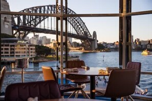 A dining area with a table and chairs, a large window with a view of a bridge and cityscape. - Terrace Boutique in the Heart of The Rocks (The Rocks)